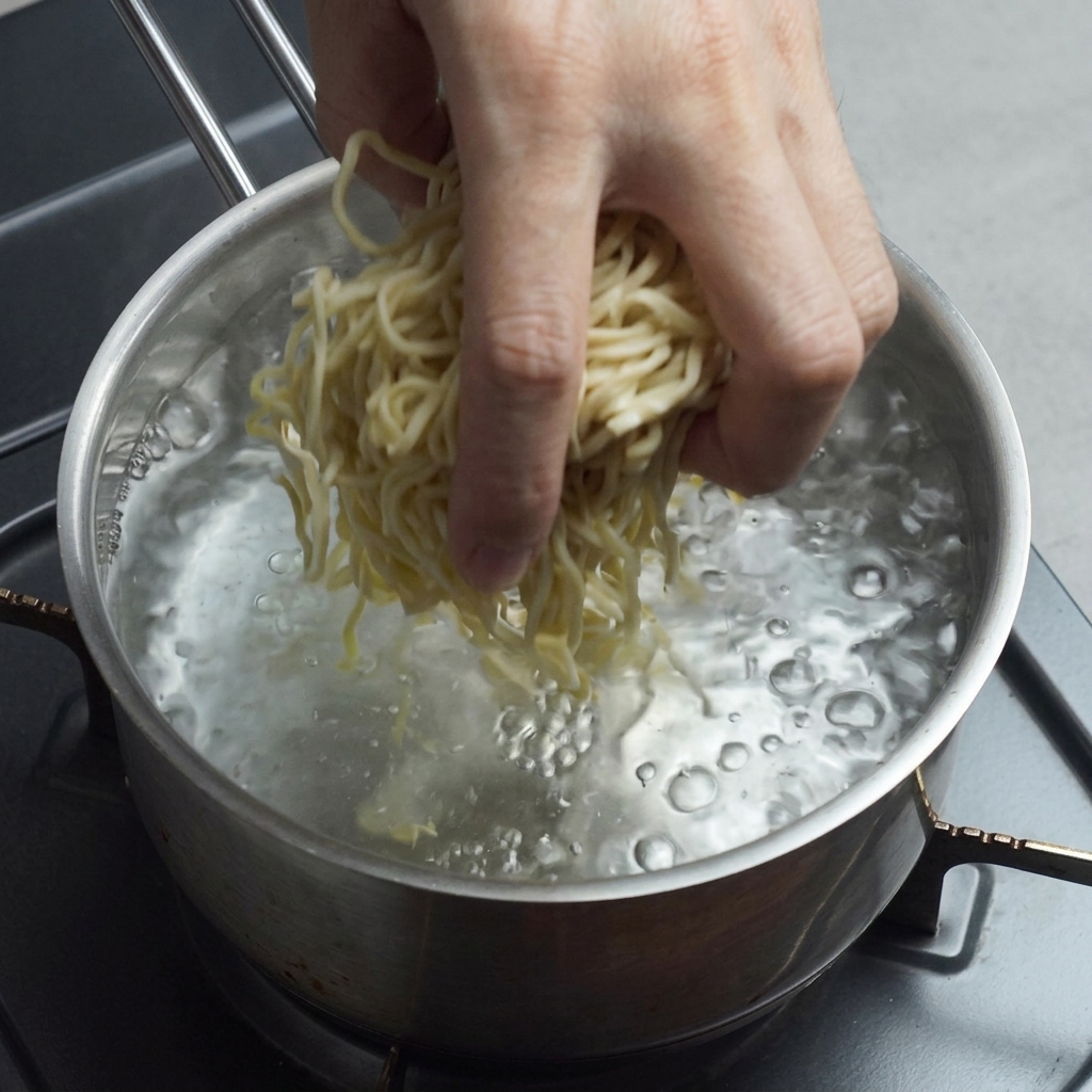 Frische gelbe Ramen-Nudeln werden in einen Topf mit sprudelnd kochendem Wasser gegeben.