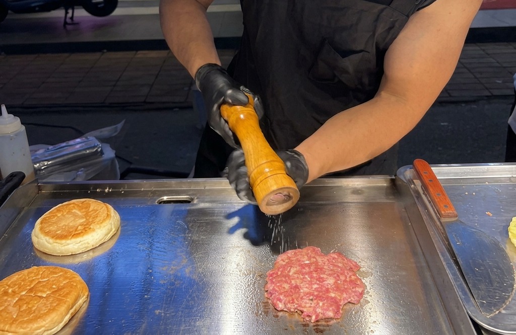 Frisches Meersalz und schwarzer Pfeffer werden aus einer Mühle auf das brutzelnde Fleisch gestreut.