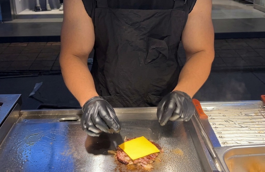 Eine Scheibe gelber Käse schmilzt auf dem heißen Fleischpatty auf der Grillplatte.