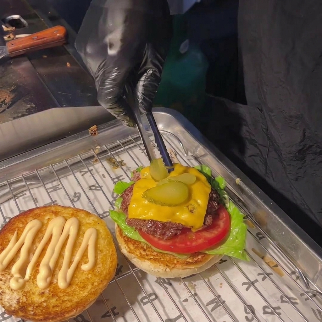 Mit einer Zange werden zwei Gurkenscheiben auf den geschmolzenen Käse gelegt.