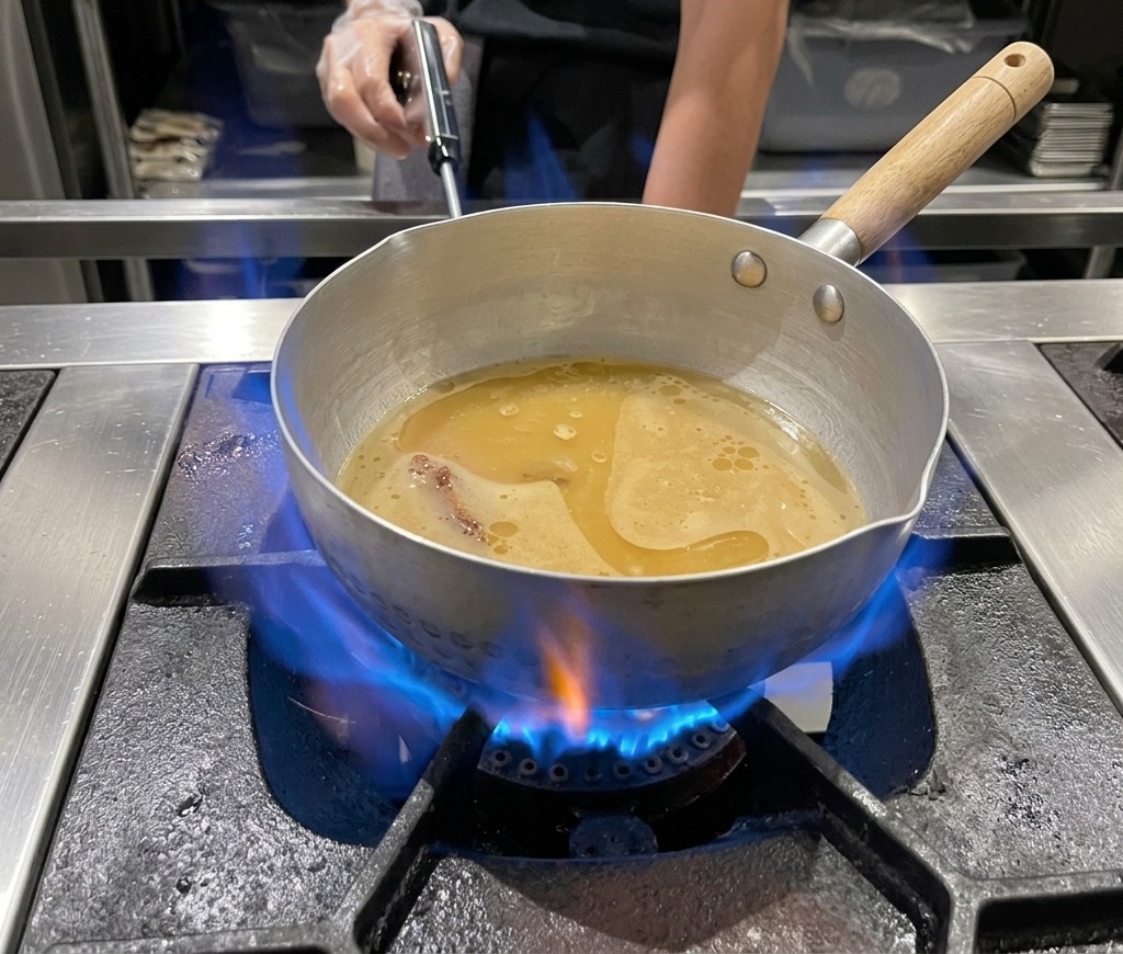 Ein Topf mit Miso-Ramen-Brühe köchelt über einer blauen Gasflamme.