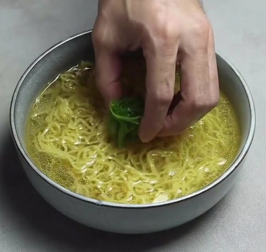 Eine Hand platziert fein geschnittene Frühlingszwiebeln auf den Ramen-Nudeln in der klaren Brühe.