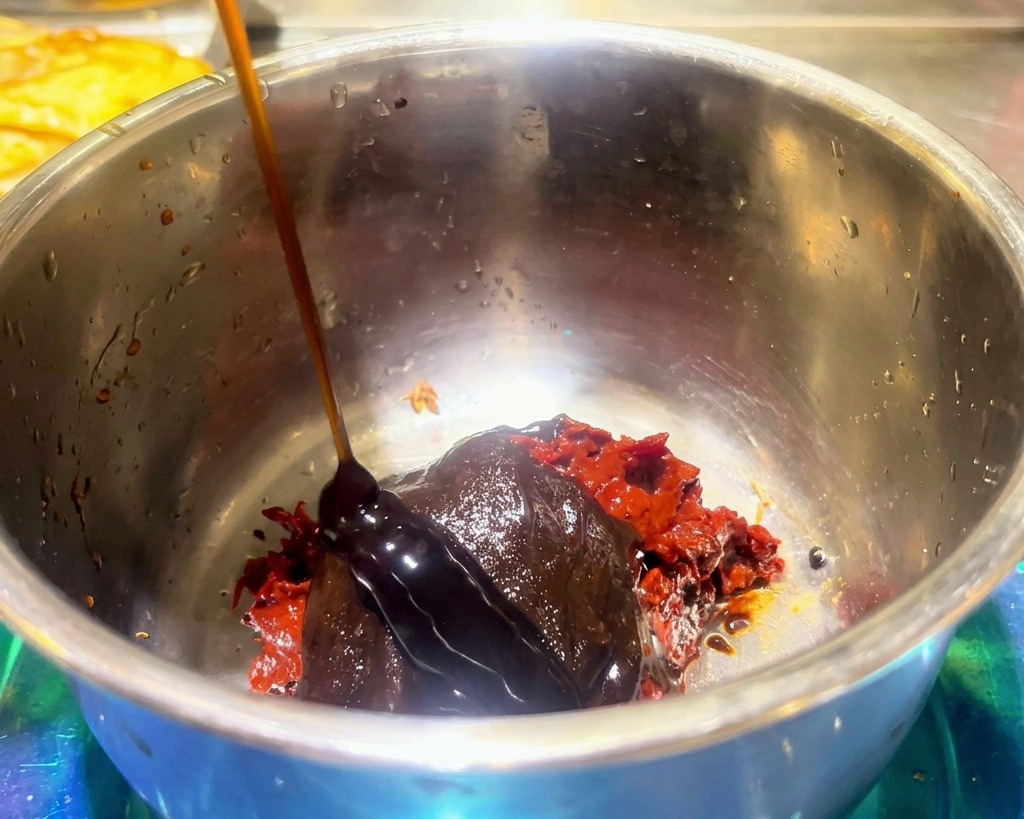 Dunkle Sauce wird über rote scharfe Bohnenpaste und Hot-Pot-Gewürz in einer Edelstahlschüssel gegossen.