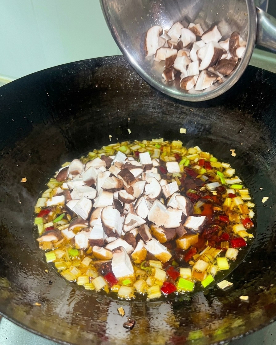 Gewürfeltes weißes Hähnchenfleisch und braune Shiitake-Pilze werden zu einer roten Sauce in einem schwarzen Wok gegeben.