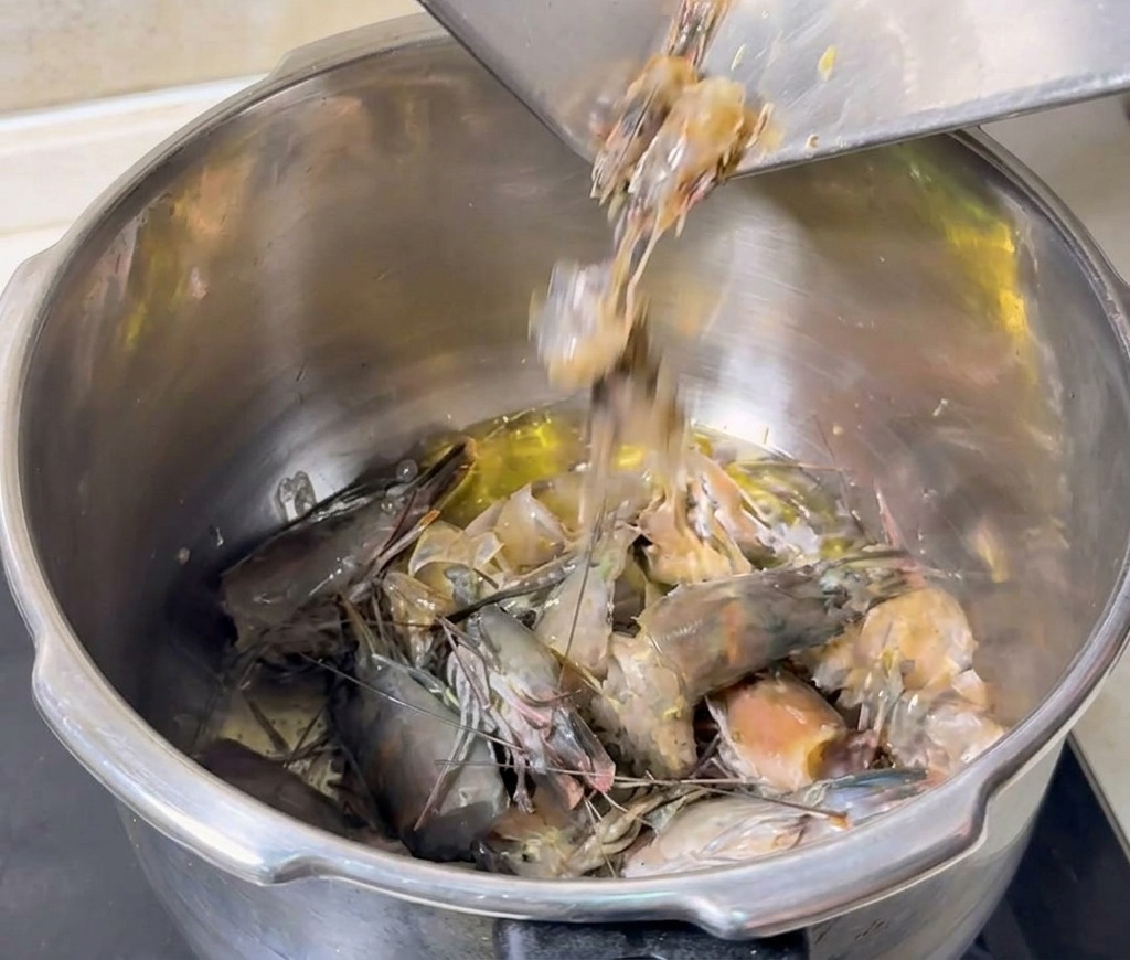 Graue Garnelenköpfe und -schalen werden aus einer Metallschale in einen Topf mit heißem Öl gegeben.