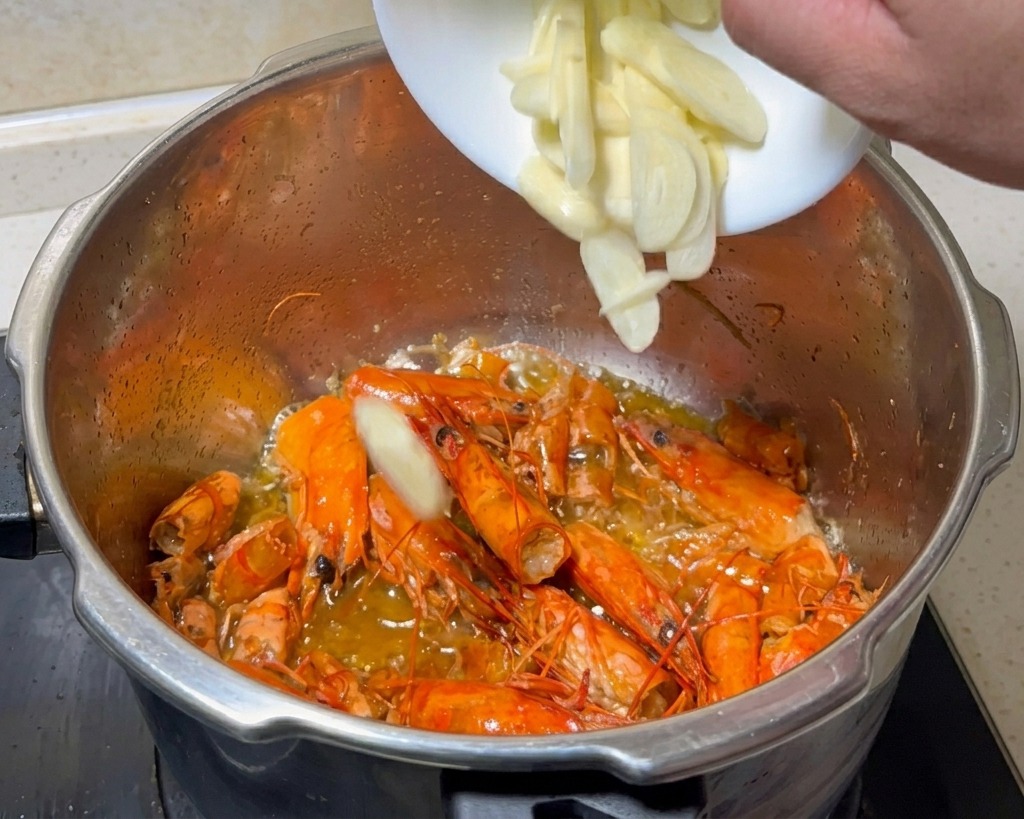 Frisch geschnittener Knoblauch wird aus einer kleinen weißen Schüssel zu den gerösteten Garnelenschalen gegeben.