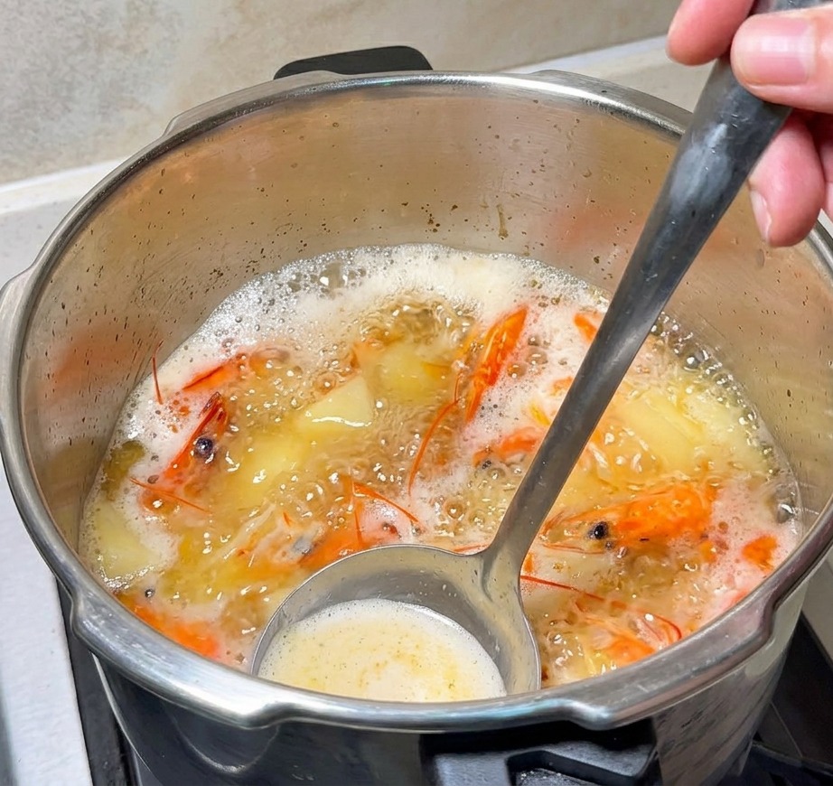 Eine Schöpfkelle rührt in der köchelnden, orangefarbenen Garnelenbrühe, während ein Stück Butter schmilzt.