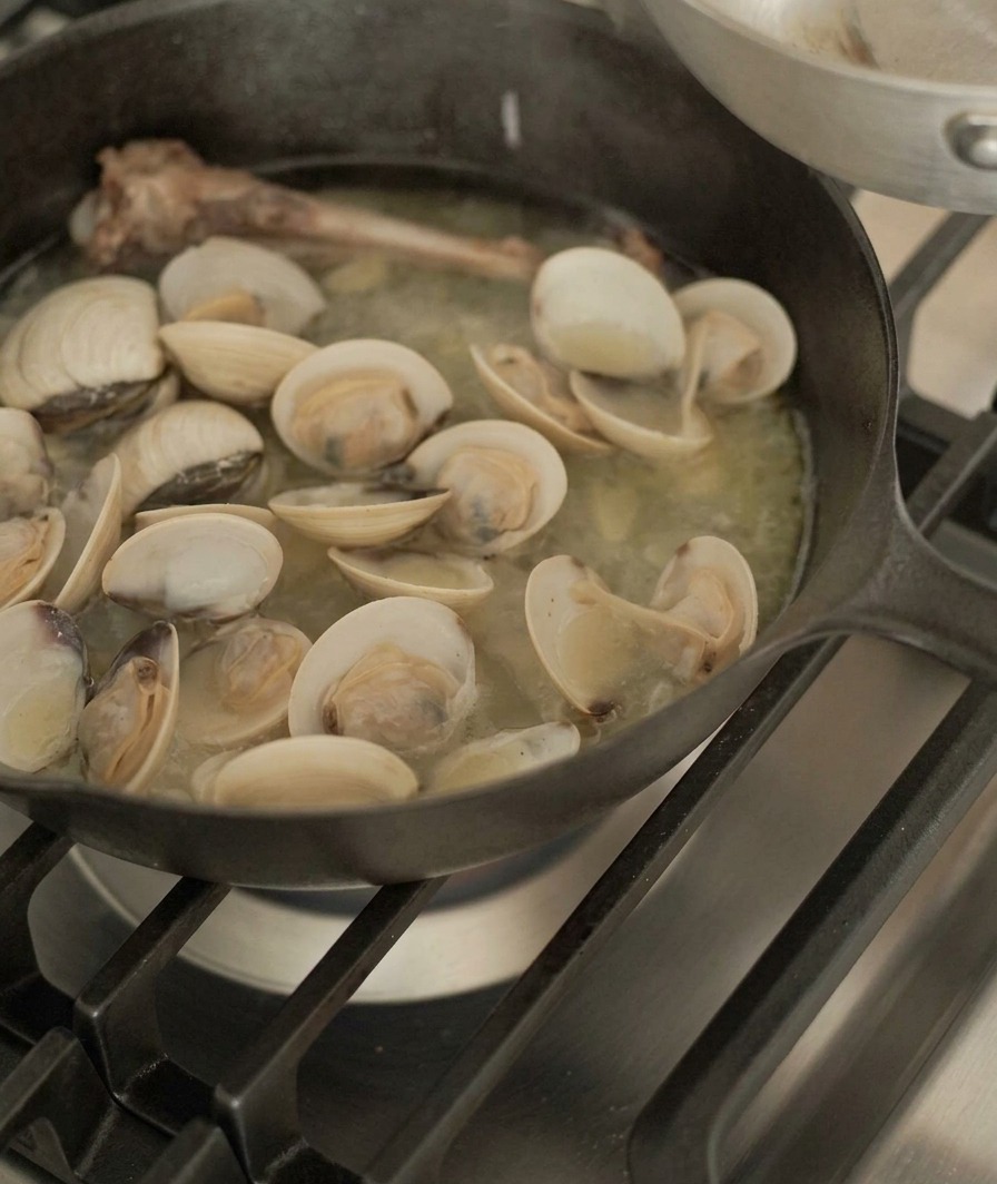 Geöffnete Muscheln werden mit einer Zange aus der Pfanne mit Entenknochen und Sud gehoben.