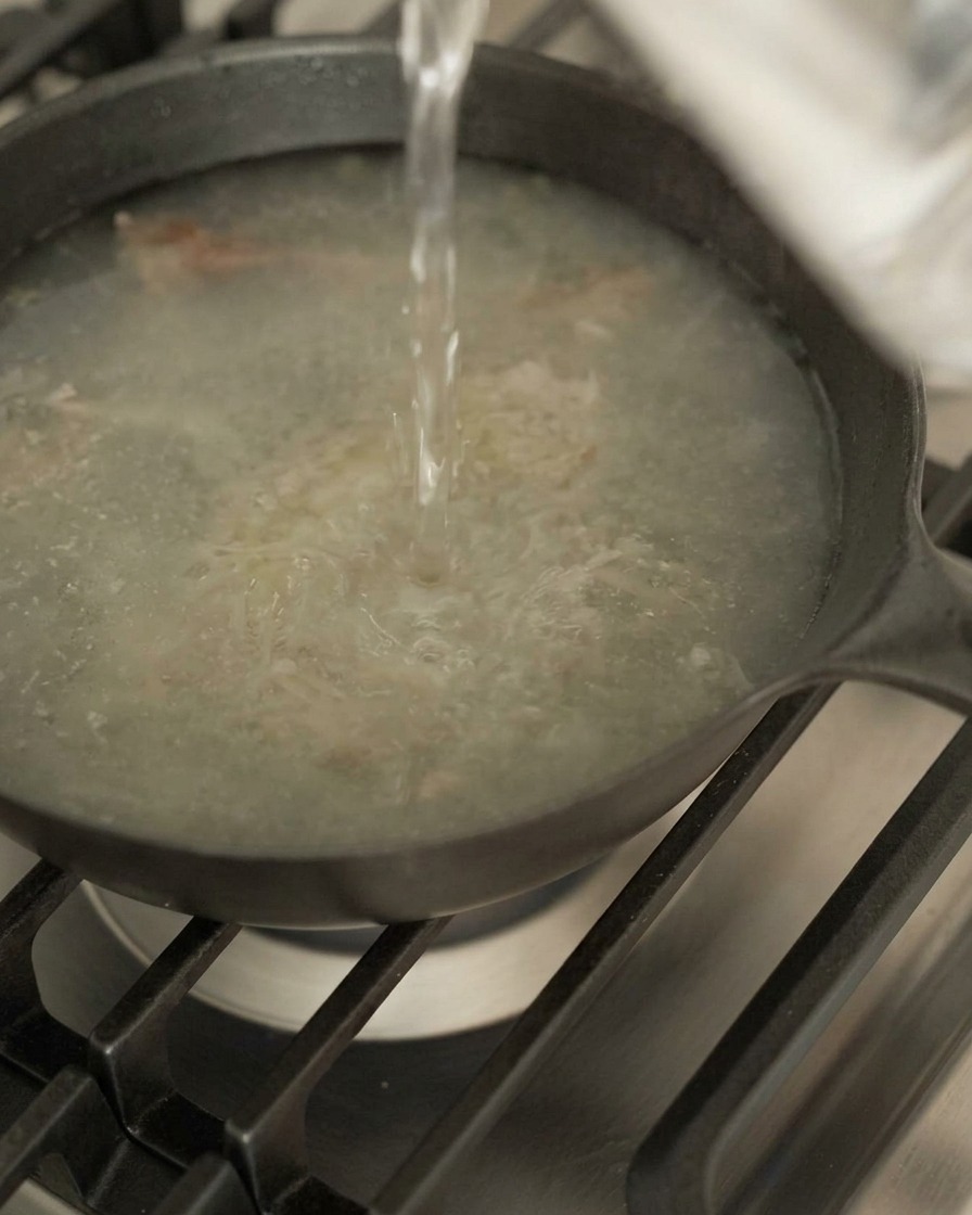 Wasser wird in die Pfanne mit dem Bratensaft und den Aromaten gegossen.