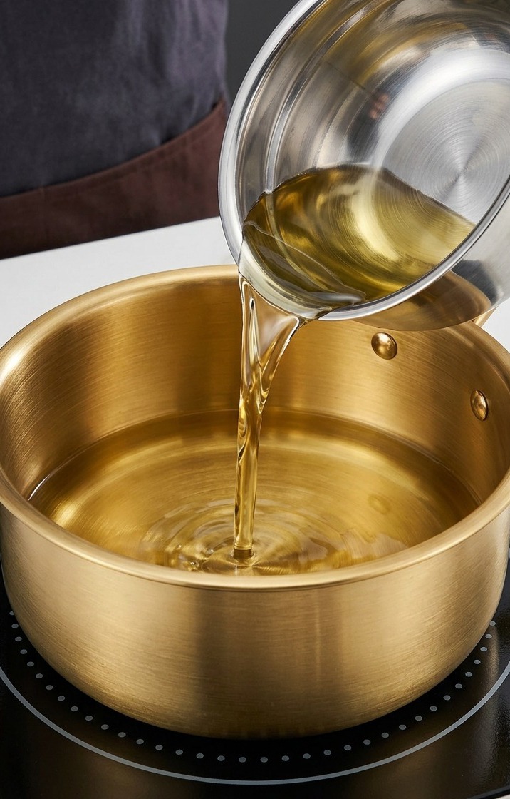 Erdnuss- und Sesamöl werden in einem goldenen Topf auf einem Induktionsherd erhitzt.