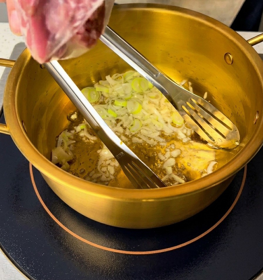 Geschnittene Frühlingszwiebeln und gehackter Knoblauch werden im Öl am Topfboden angebraten.