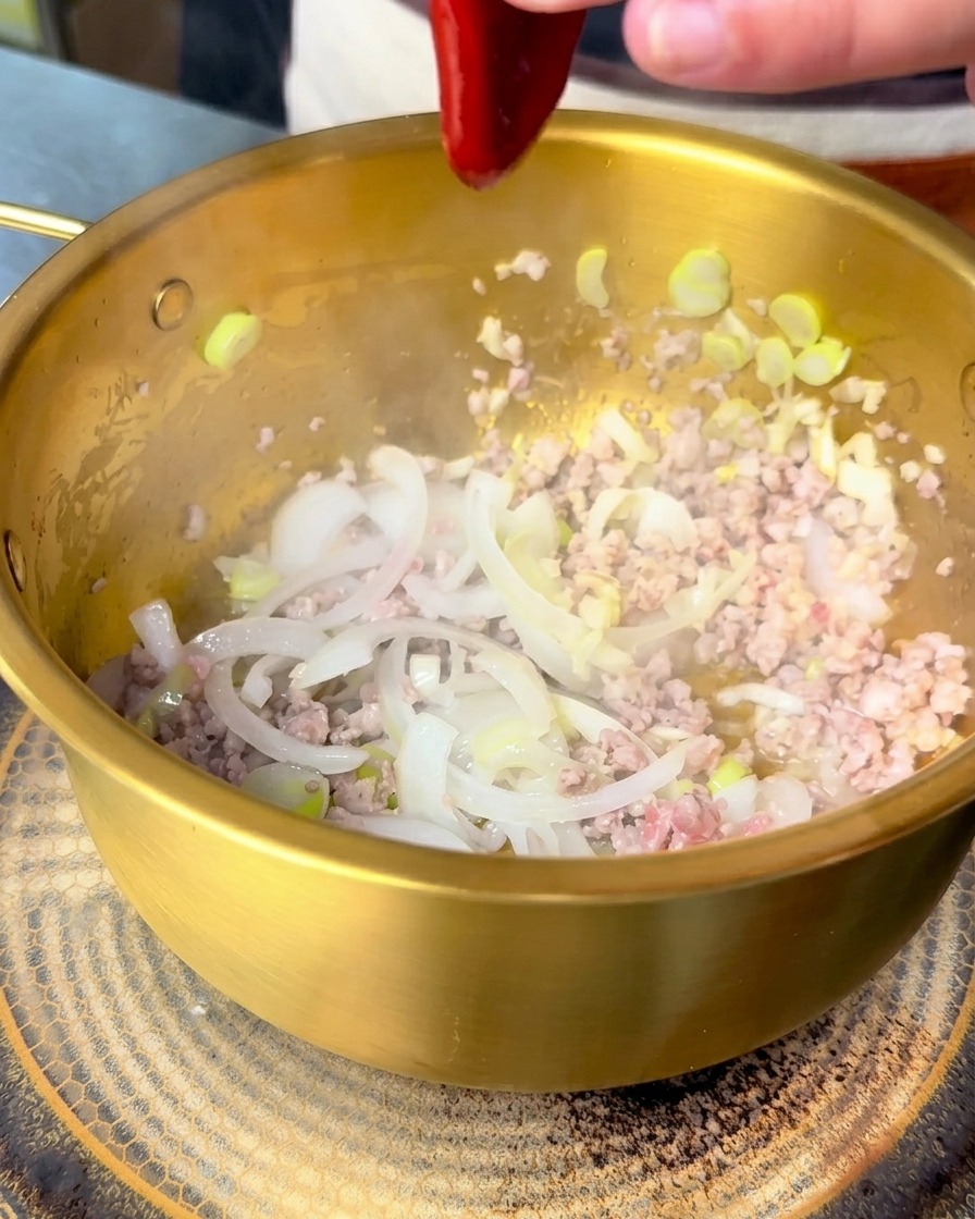 Rote koreanische Bibimbap-Sauce wird in den Topf zu Fleisch und Zwiebeln gegeben.