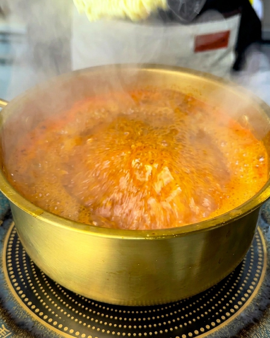 Ein Block getrockneter Instant-Ramen wird in die sprudelnd kochende rote Suppe getaucht.