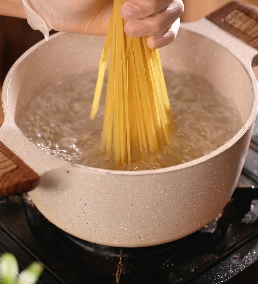 Trockene Spaghetti werden in einen Topf mit kochendem Wasser gegeben.