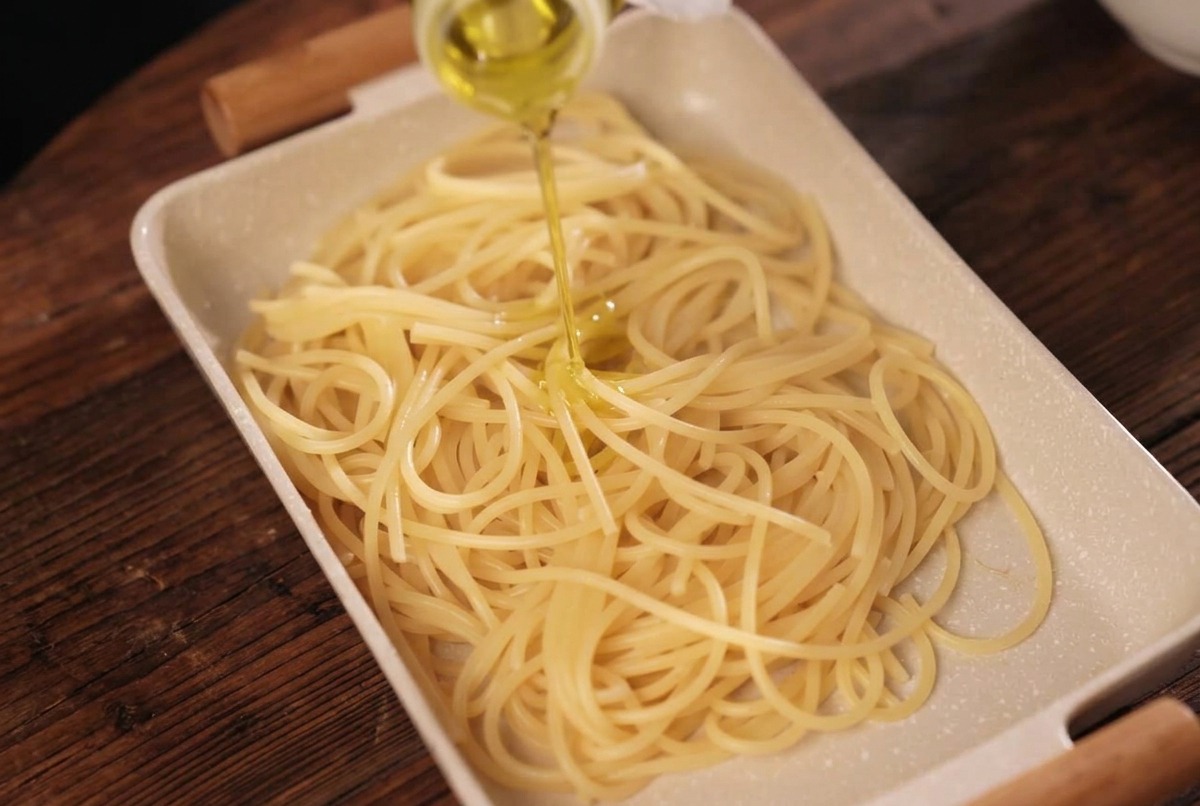 Gekochte Spaghetti in einer Schale, die mit gelbem Olivenöl aus einer Flasche beträufelt werden.