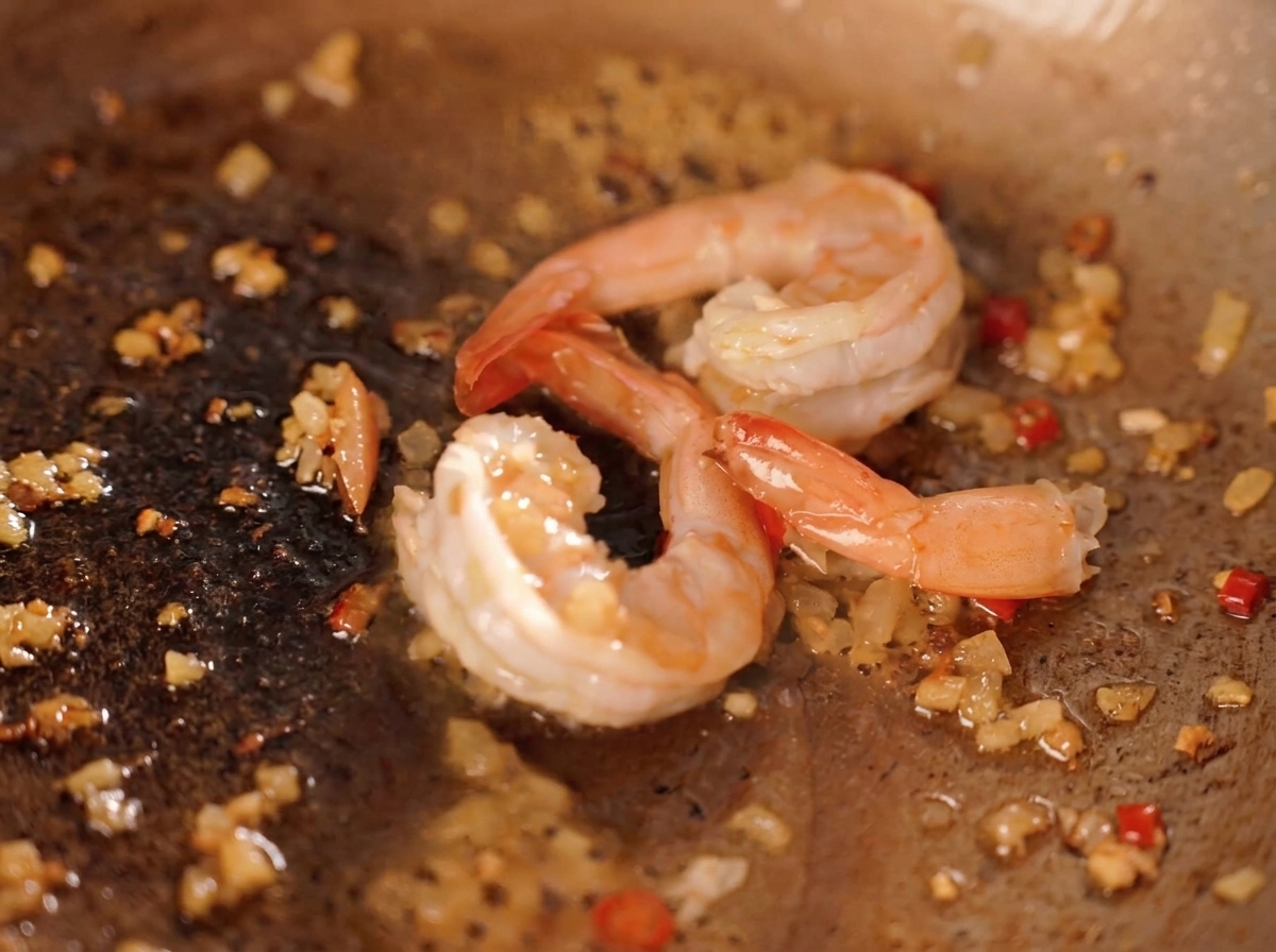 Garnelen werden mit gehackten Chilis, Zwiebeln und gelbem Eigelb-Gekrümel in der Pfanne gebraten.