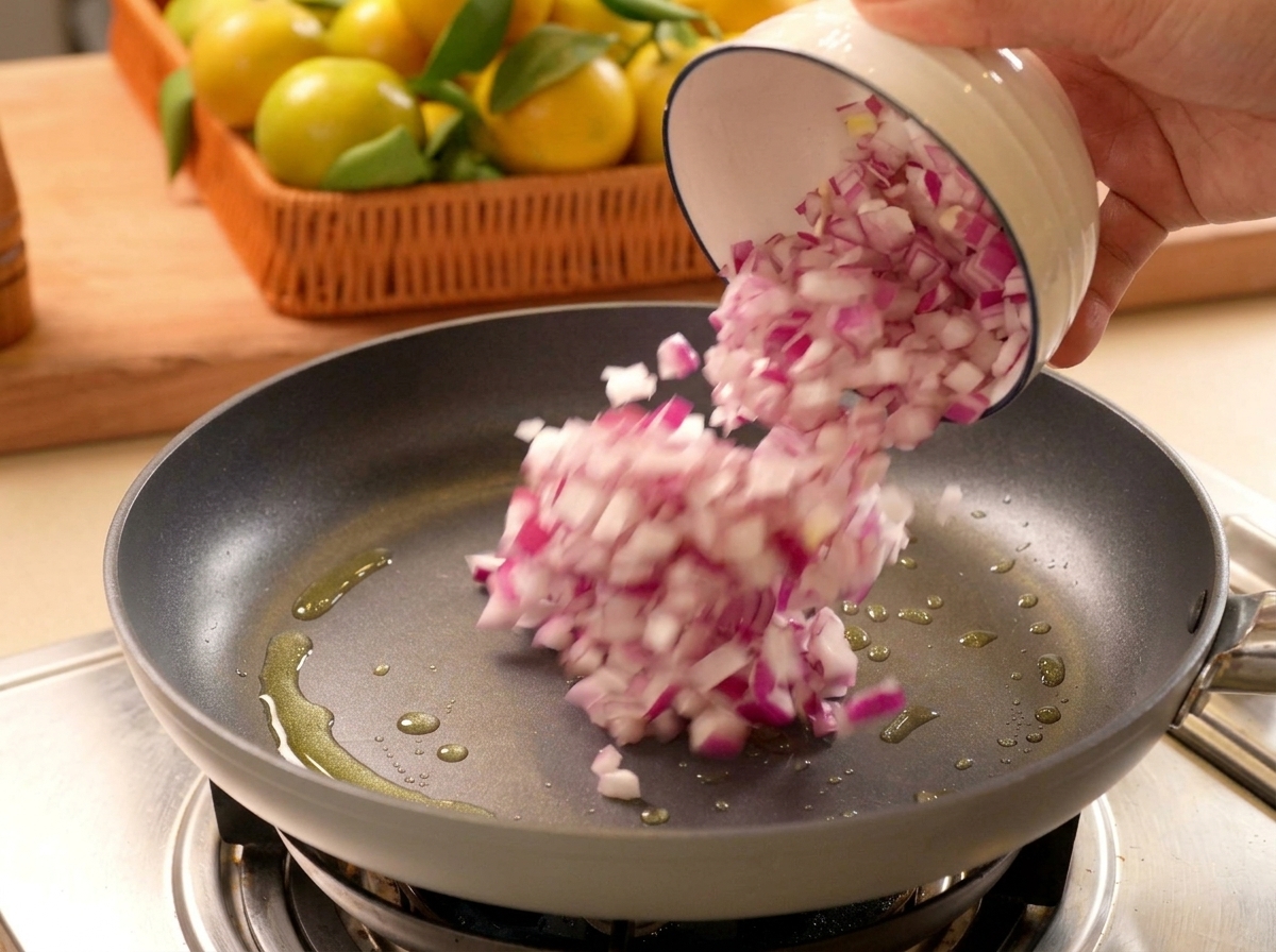 Gehackte rote Zwiebeln werden aus einer weißen Schale in eine erhitzte Pfanne mit Öl gegeben.