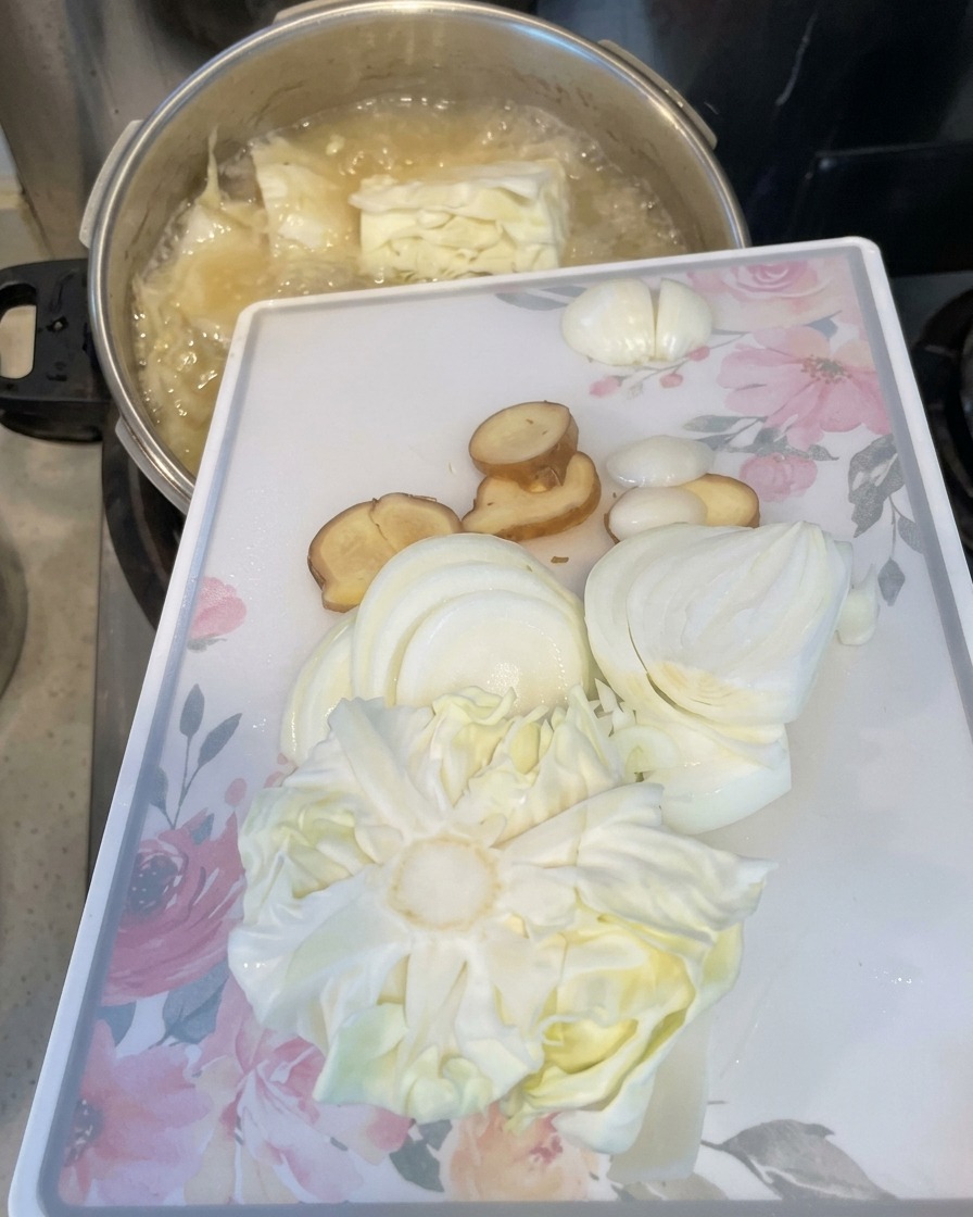 Zwiebeln, Ingwer und Kohl werden von einem Schneidebrett in den kochenden Topf gegeben.