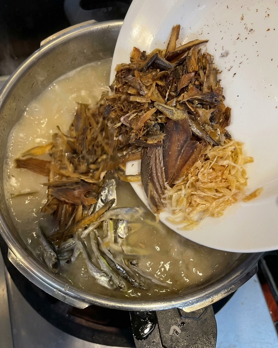 Fischflocken, kleine Sardinen und getrocknete Garnelen werden in die cremige Brühe gegeben.