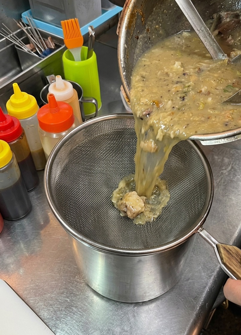 Cremige Ramen-Brühe wird durch ein Metallsieb gegossen, um Feststoffe aufzufangen.