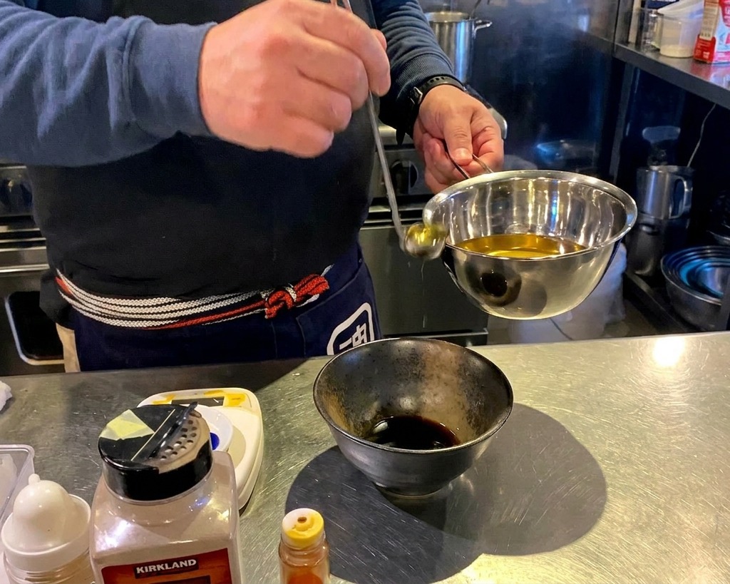 Goldenes Öl wird aus einer Kelle in eine Schüssel mit dunkler Würzsauce gegossen.