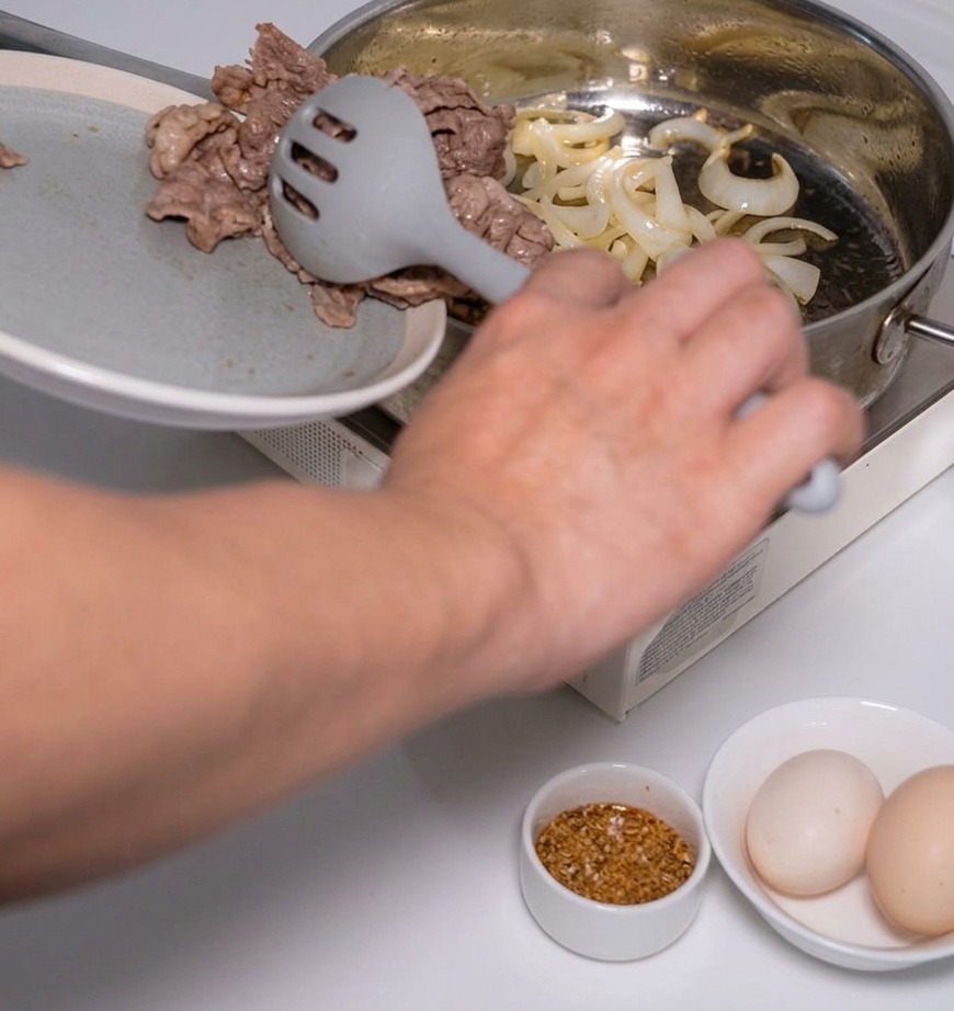 Blanchiertes Fleisch wird mit einem Schaumlöffel zu den gedünsteten Zwiebeln in die Pfanne gegeben.