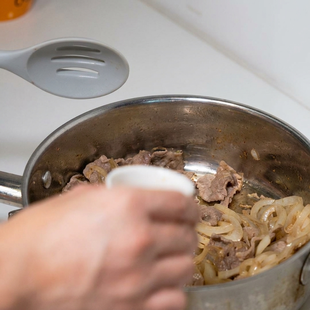 Eine vorgemischte dunkle Sauce wird über das Fleisch und die Zwiebeln in der Pfanne gegossen.