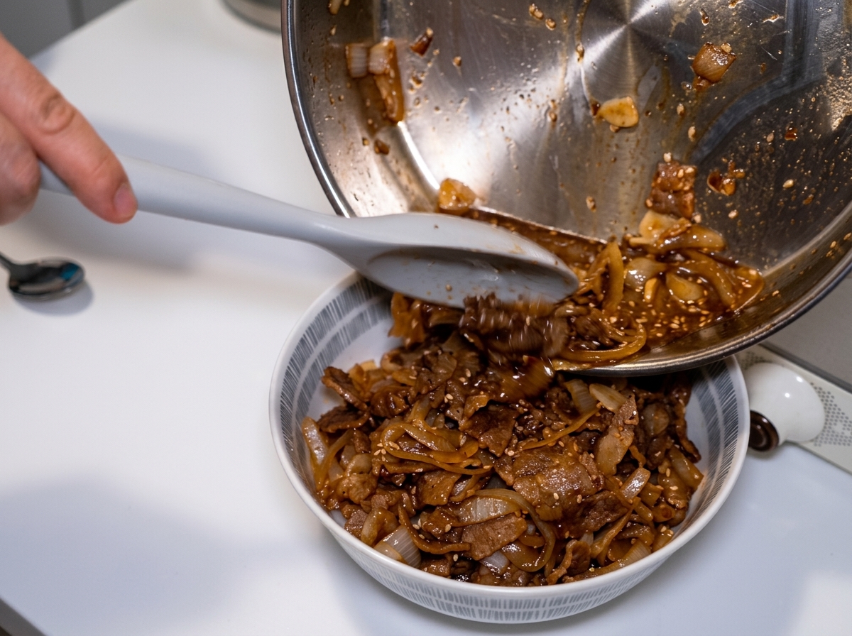 Die Pfanne wird gekippt, um die restliche Sauce und Zwiebeln mit einem Pfannenwender über die Reisbowl zu geben.