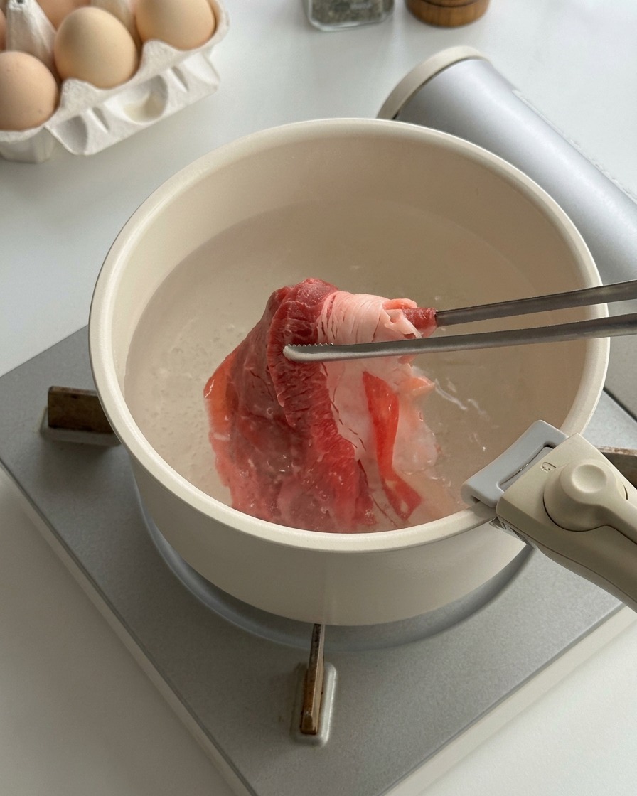 Hauchdünne rohe Rindfleischscheiben werden mit Metallstäbchen in einem Topf mit kochendem Wasser blanchiert.