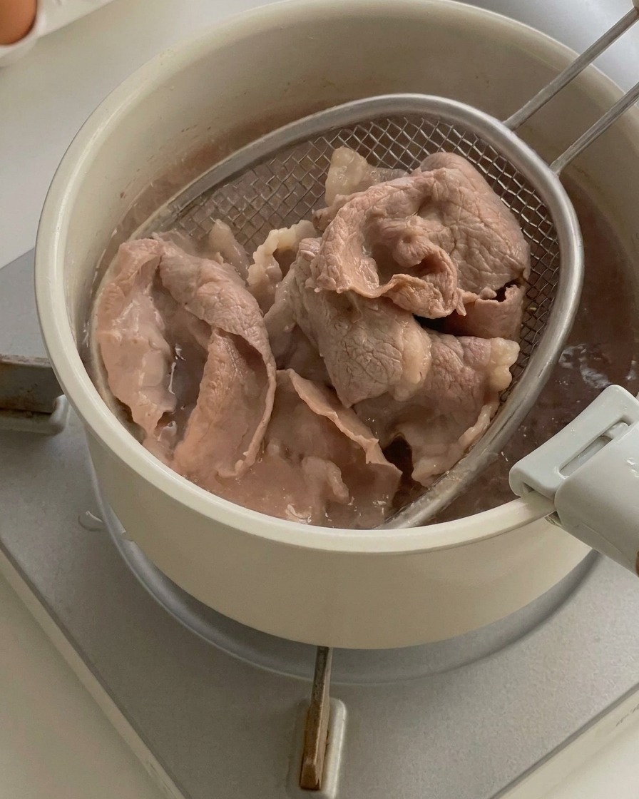 Gekochte Rindfleischscheiben werden mit einem Schaumlöffel aus dem kochenden Wasser gehoben.