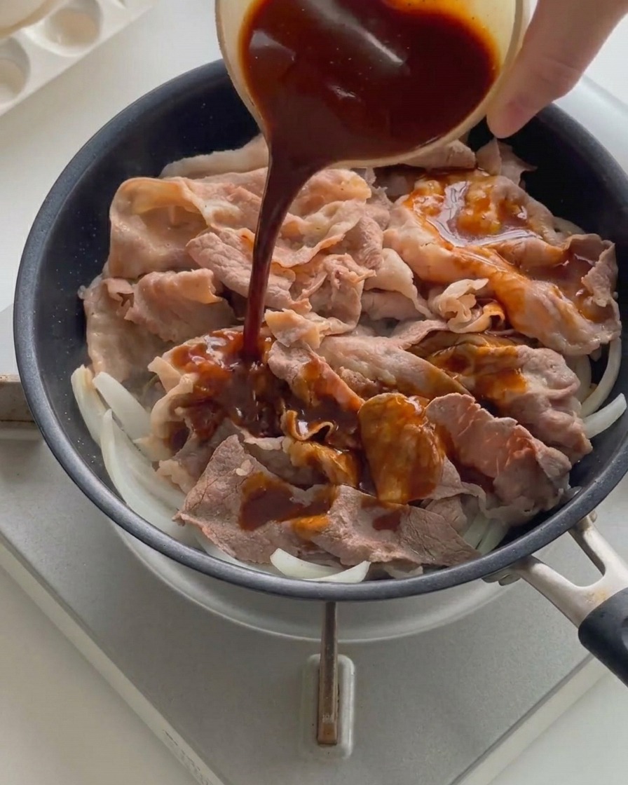 Dunkle Sauce wird aus einer kleinen Schüssel über Fleisch und Zwiebeln in der heißen Pfanne gegossen.