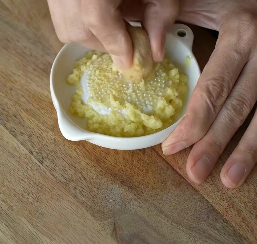 Frischer Ingwer wird auf einer weißen Keramikreibe zu einer feinen Paste gerieben.
