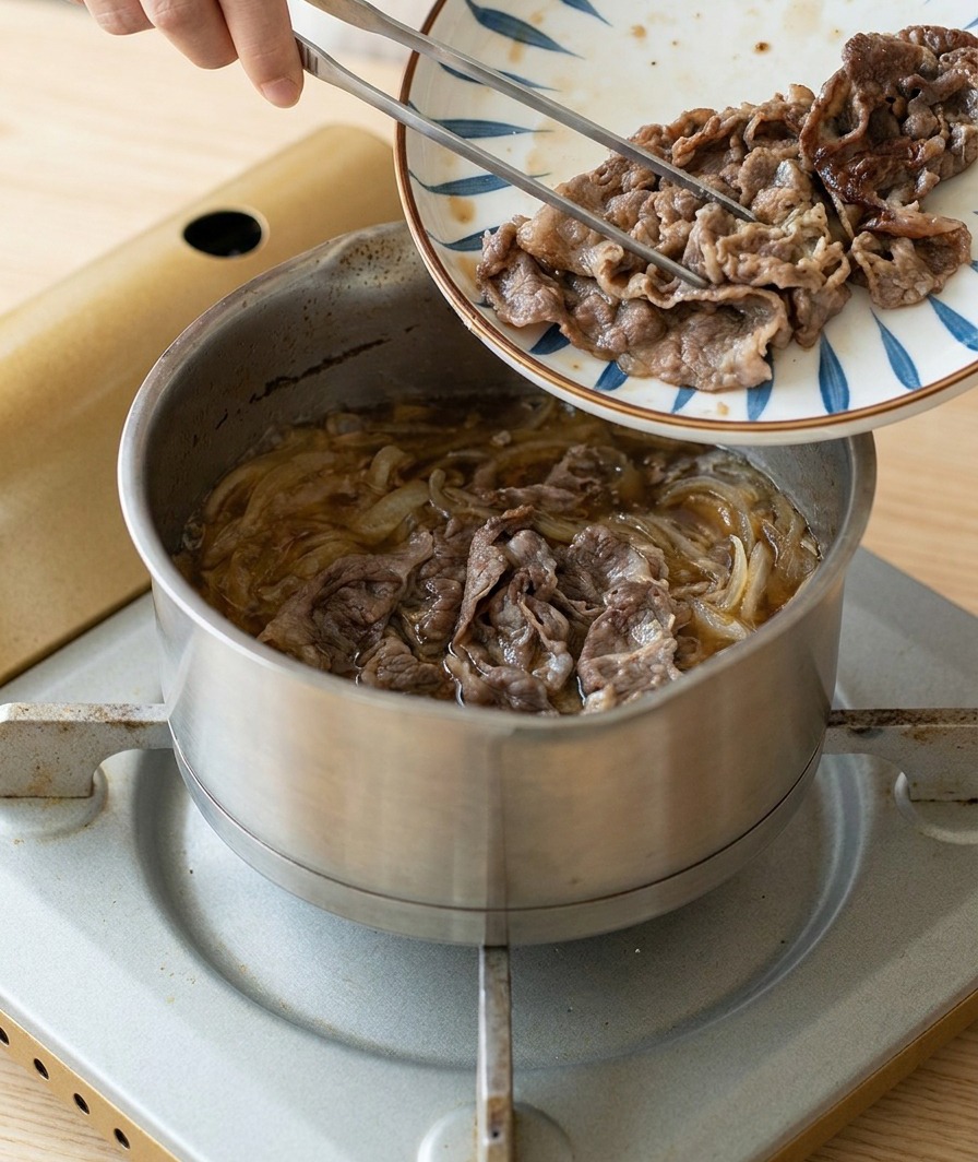 Angebratene Rindfleischscheiben werden von einem Musterteller in den Topf zu den köchelnden Zwiebeln und der Sauce gegeben.