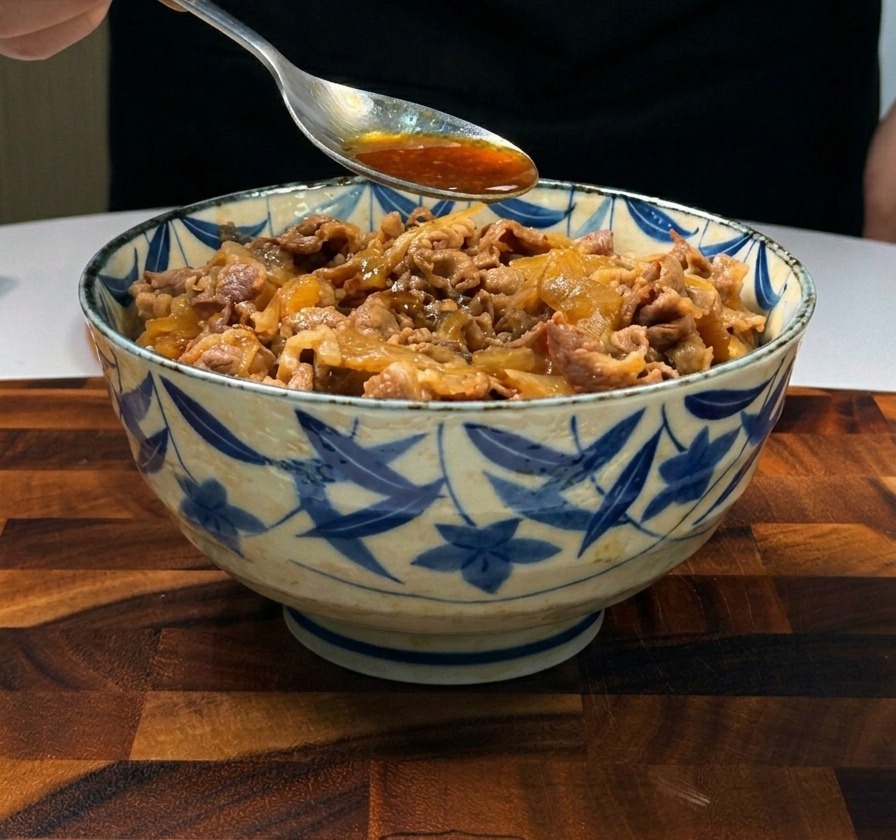 Ein Metalllöffel gießt dunkle, herzhafte Sauce über in Scheiben geschnittenes Rindfleisch und Zwiebeln, die auf Reis angerichtet sind.
