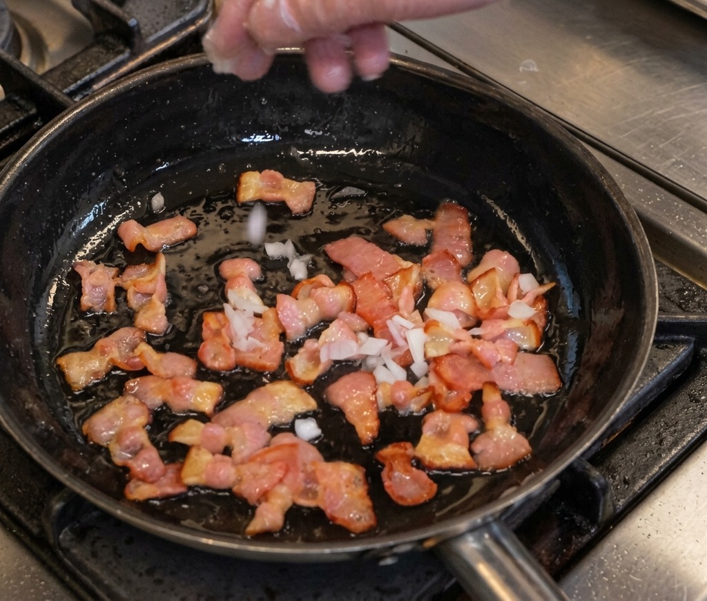 Gewürfelte Zwiebeln werden zum Speck in die Pfanne gegeben.