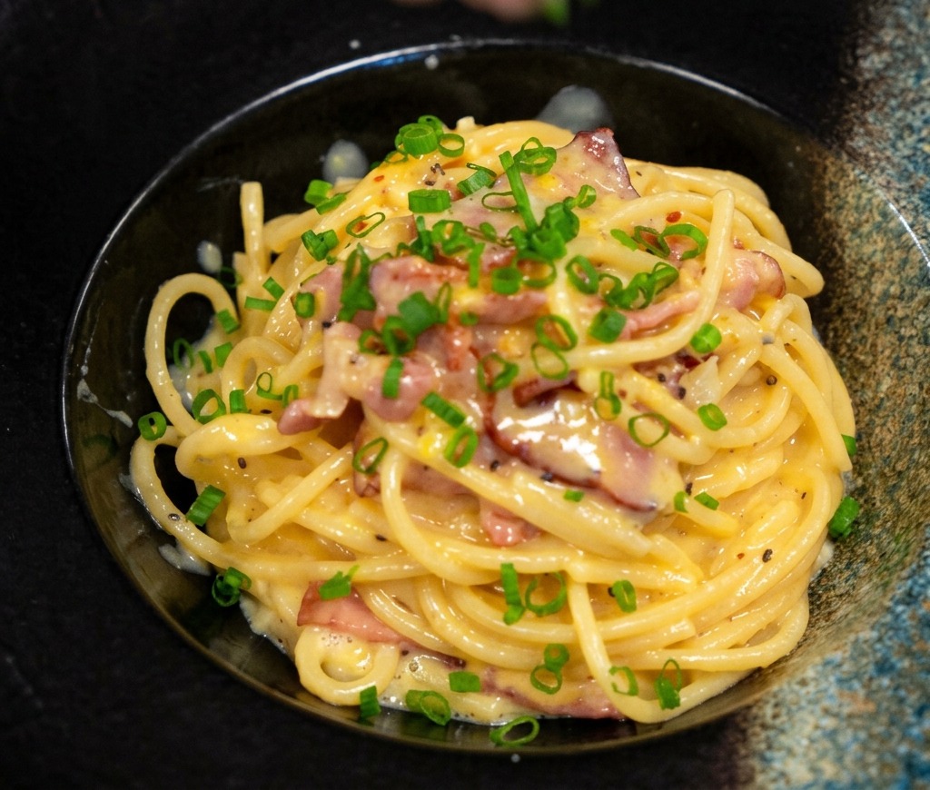 Frühlingszwiebeln werden über eine Portion cremige Pasta gestreut.