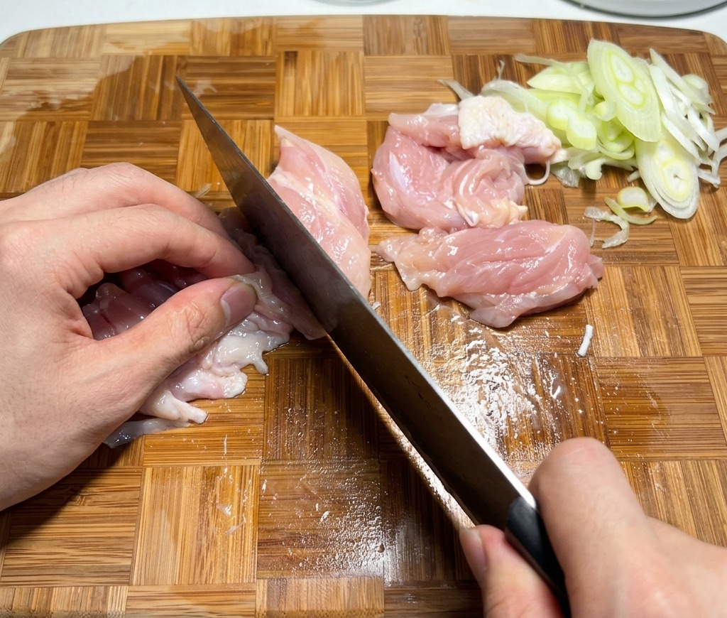 Rohe Hähnchenoberkeulen werden auf einem Holzschneidebrett in mundgerechte Stücke geschnitten.