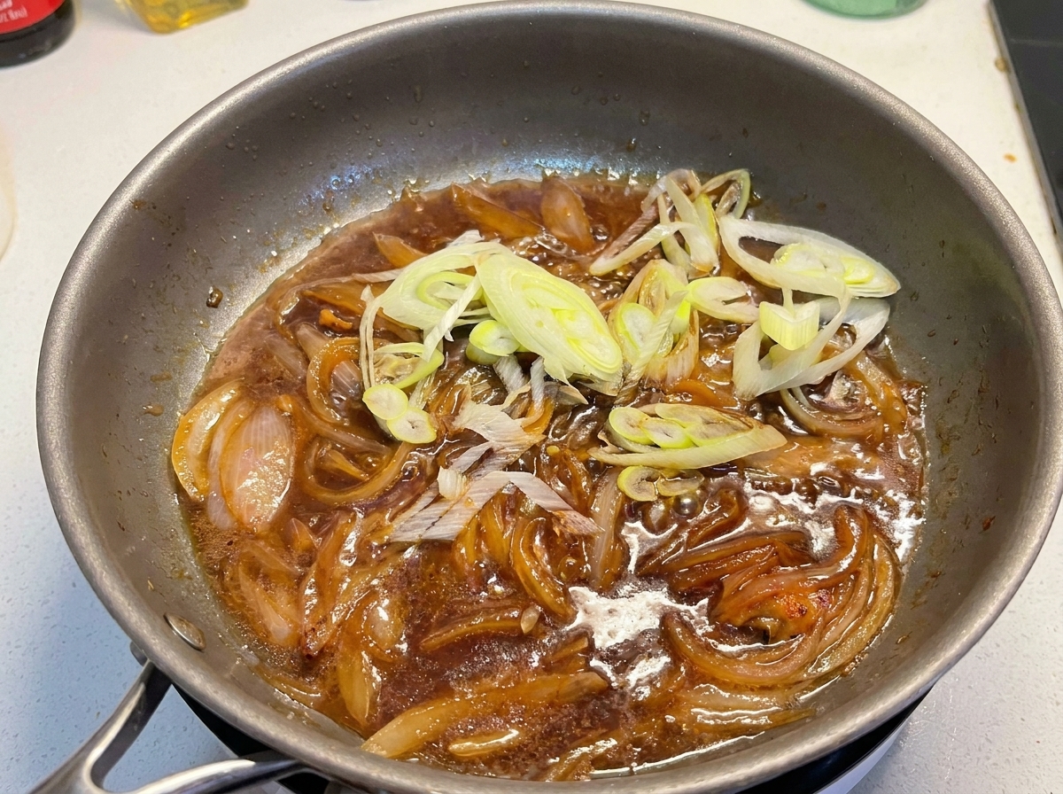 Geschnittene Frühlingszwiebeln werden in die Pfanne zu der köchelnden Sauce und den weichen Zwiebeln gegeben.