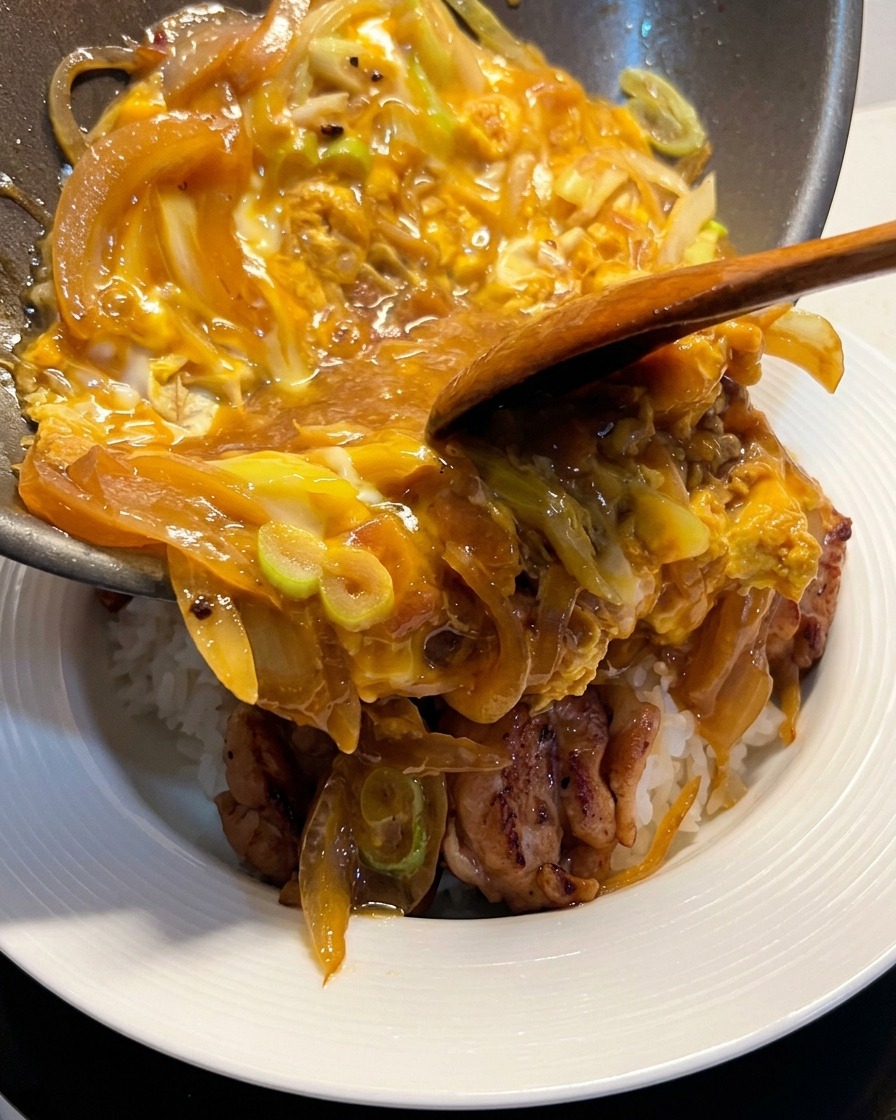 Die saftige Ei-Zwiebel-Mischung wird aus der Pfanne direkt auf die Reisbowl mit dem Hähnchen gleiten gelassen.