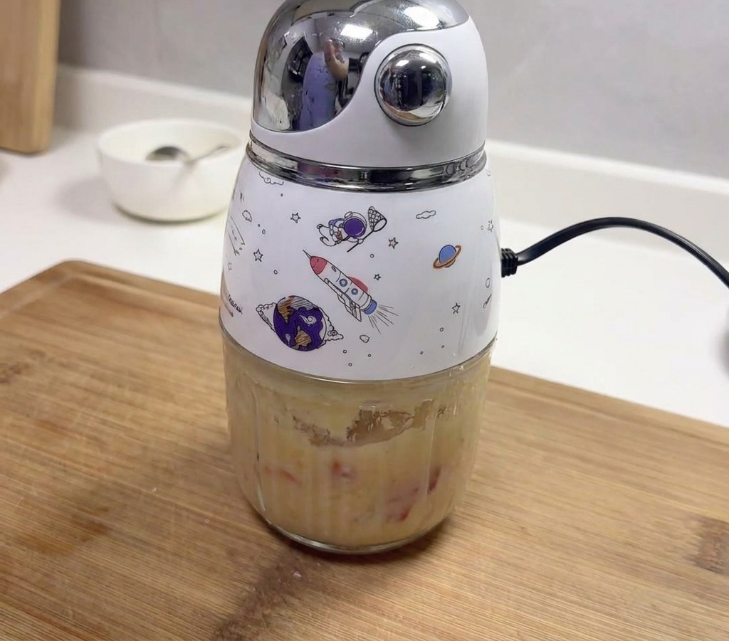 Ein kleiner elektrischer Mixer mit Weltraum-Motiven enthält eine dicke Paste aus gemischtem Knoblauch und roten Chilis.