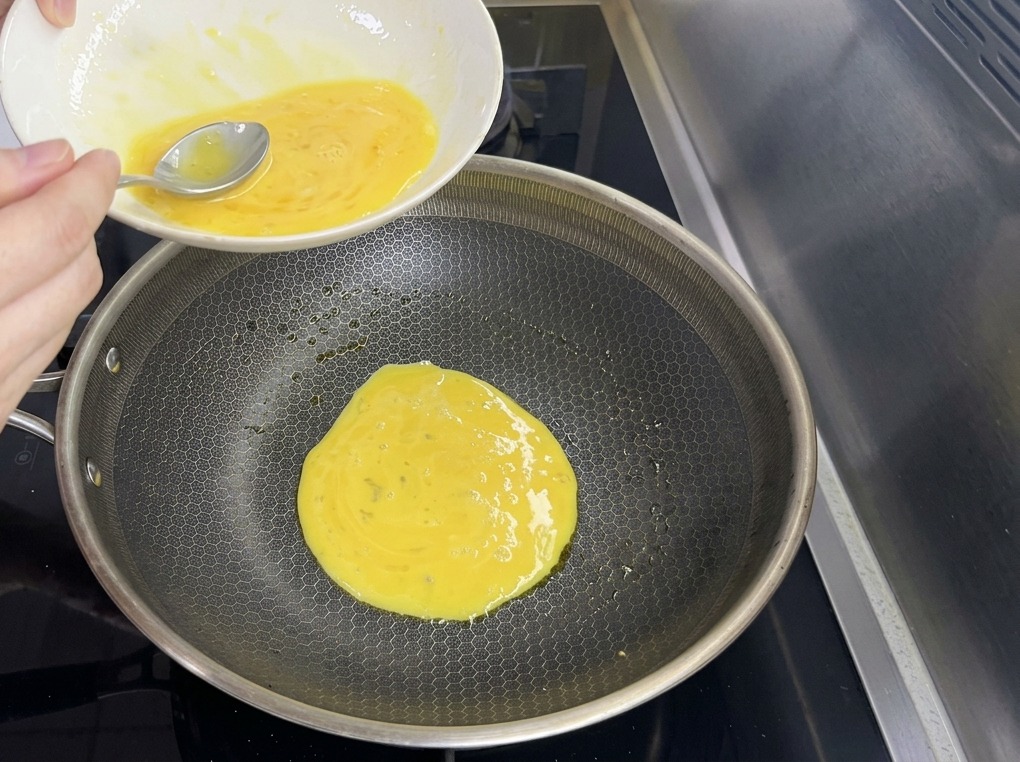 Dünner gelber Eierteig wird aus einer Schüssel in eine große Bratpfanne mit Wabenmuster gegossen.