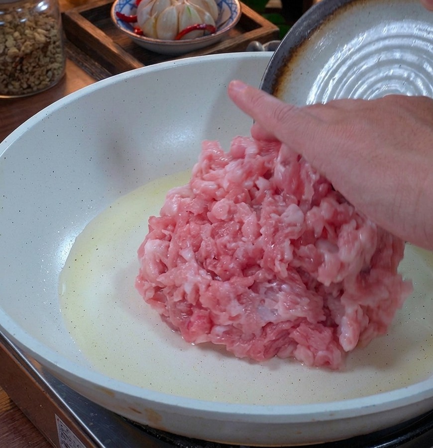 Frisches rosa Schweinehackfleisch wird in eine weiße Keramikpfanne mit etwas Öl gegeben.