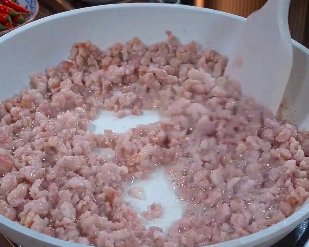 Schweinehackfleisch wird mit einem weißen Pfannenwender gerührt, während es sich von rosa zu leicht grau verfärbt.