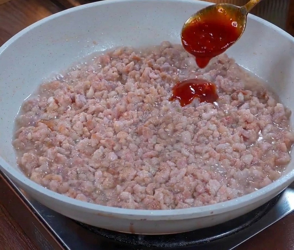 Ein Metalllöffel gießt eine dicke, dunkelbraune Sauce über das angebratene Hackfleisch in der Pfanne.