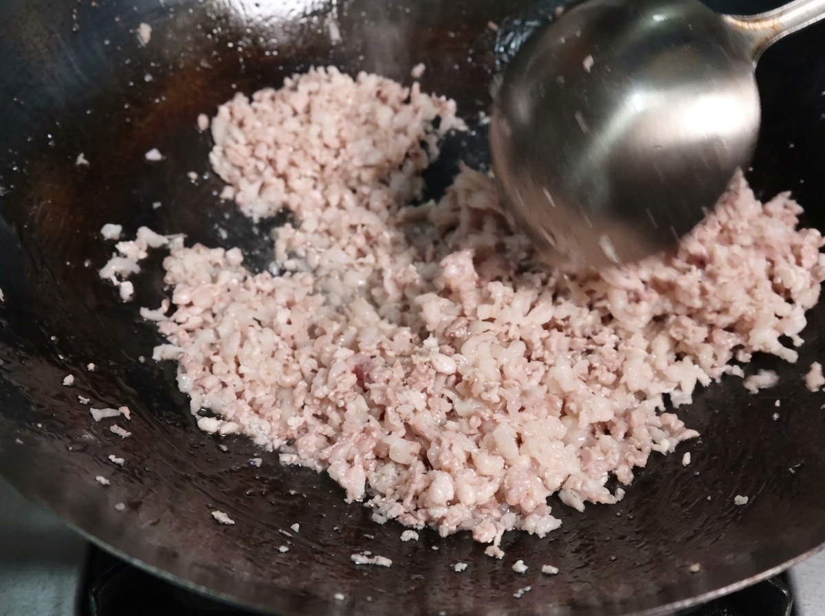 Schweinehackfleisch, das mit einer Kelle in einem heißen Wok gebraten wird und sich in feine Krümel teilt.