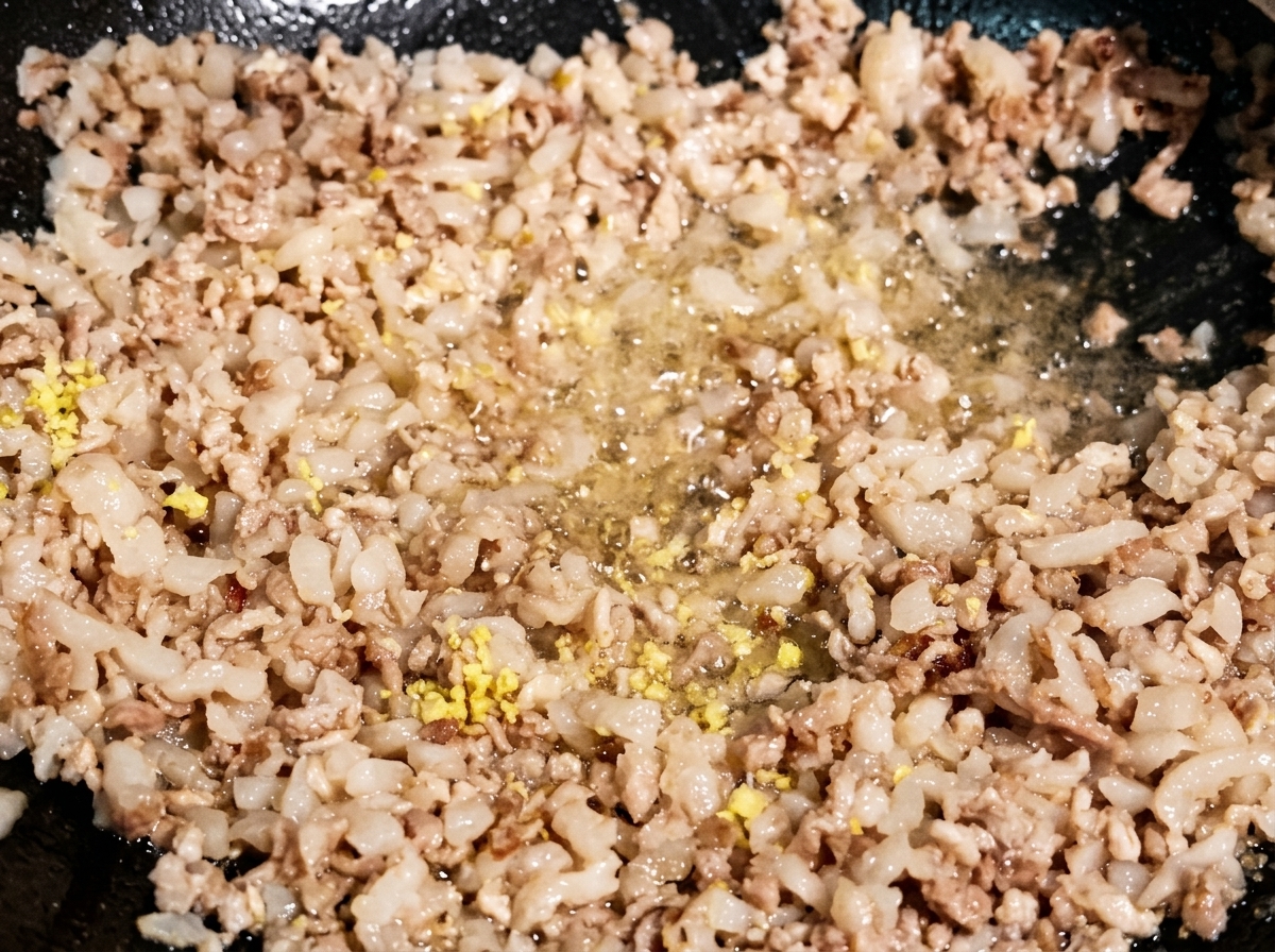 Feingehackter Ingwer und Knoblauch werden unter das gebräunte Hackfleisch in einem dunklen Wok gemischt.