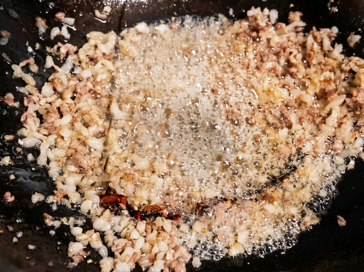 Helle Sojasauce wird in den Wok zum brutzelnden Hackfleisch gegossen.