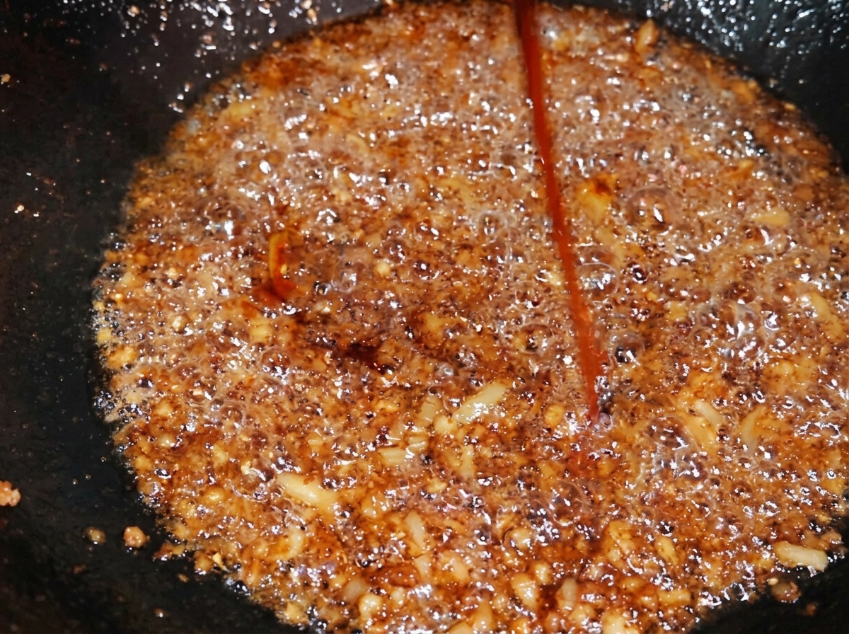 Dunkle Sojasauce wird über das gewürzte Hackfleisch gegossen, wodurch sich die Farbe intensiviert.