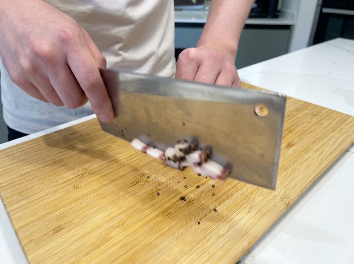 Ein Koch schneidet fette Streifen von luftgetrocknetem Guanciale mit einem großen Messer in kleine Würfel auf einem Bambusschneidebrett.