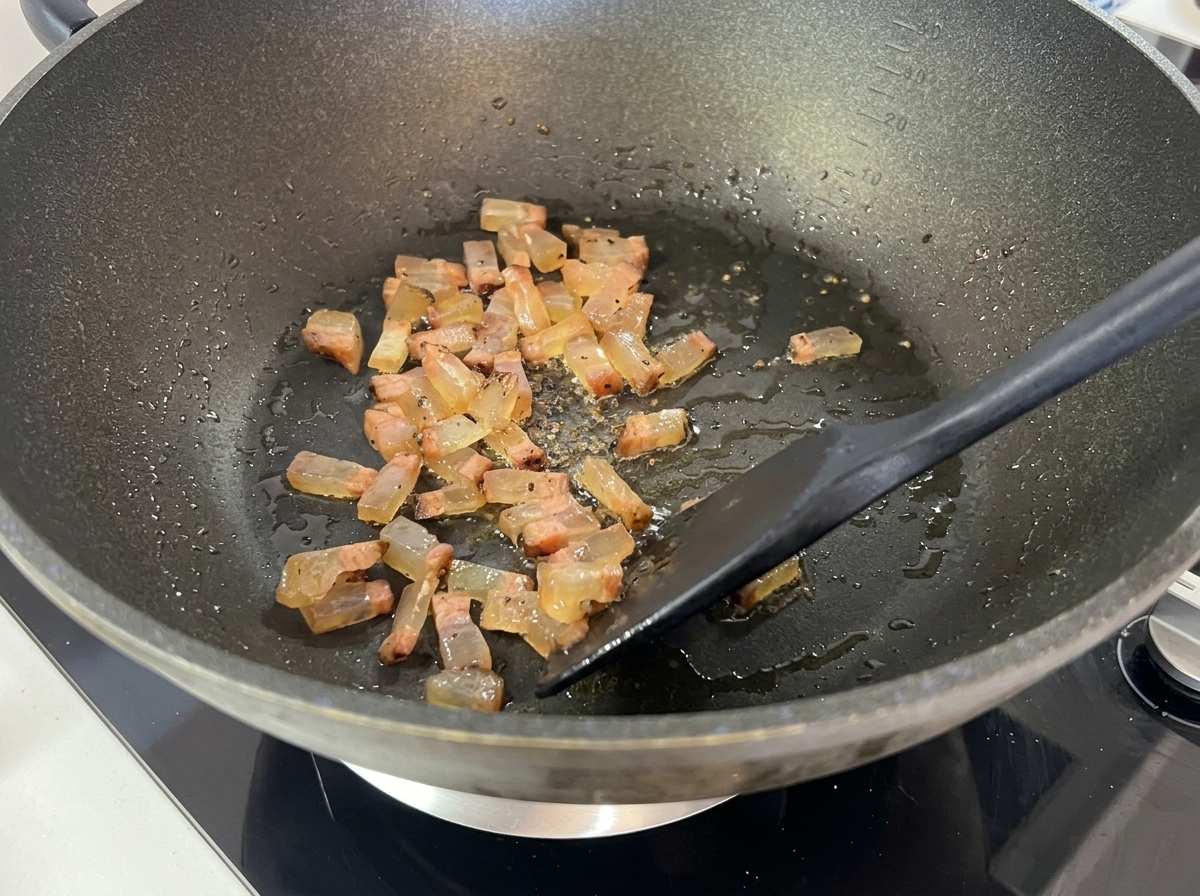 Gewürfelter Guanciale bräunt im Wok, wird glasig und setzt flüssiges Fett frei.